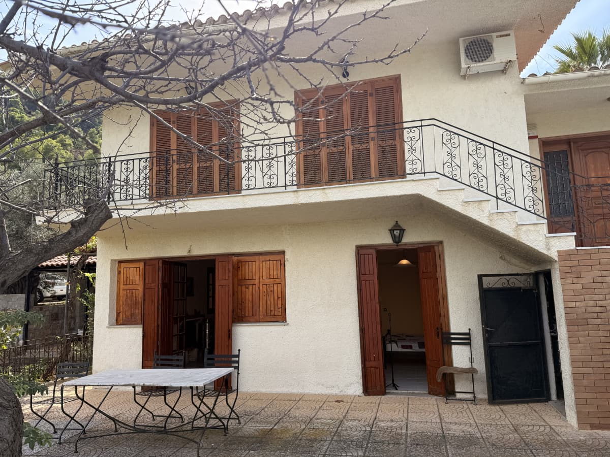 Εξωτερική άποψη διώροφου σπιτιού με καφέ ξύλινα παντζούρια, βεράντα, μπαλκόνι και εξωτερική σκάλα.
