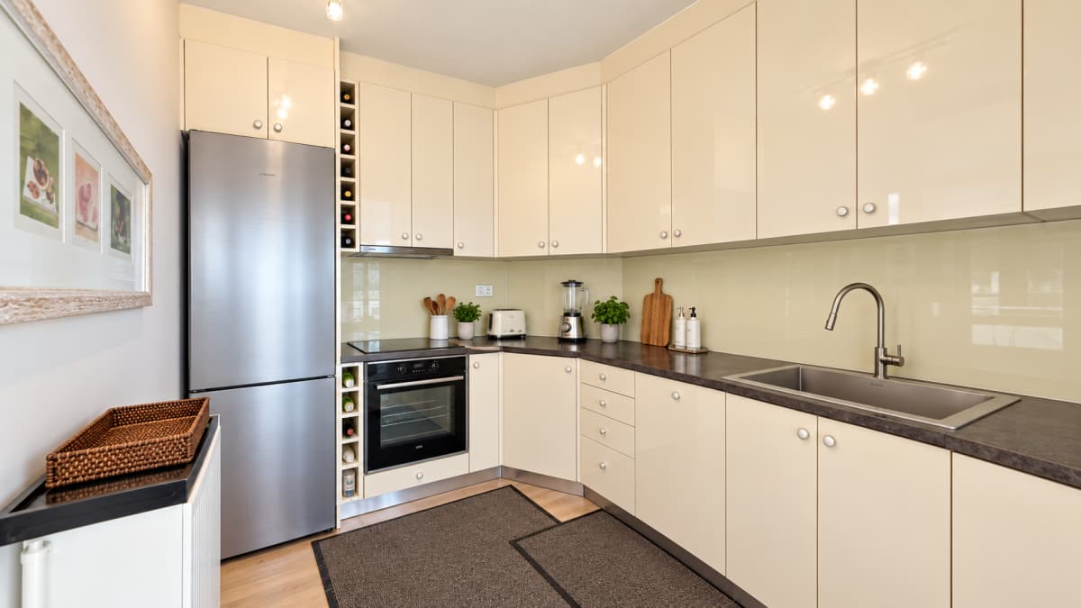 A modern kitchen features cream-colored cabinets, dark countertops, a stainless steel refrigerator and oven, and a built-in wine rack.