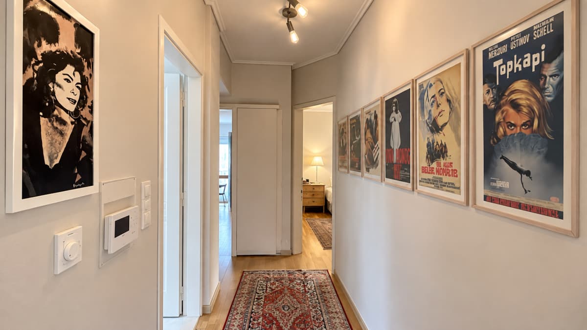 An indoor hallway with beige walls, framed movie posters, a doorway, and a runner rug.