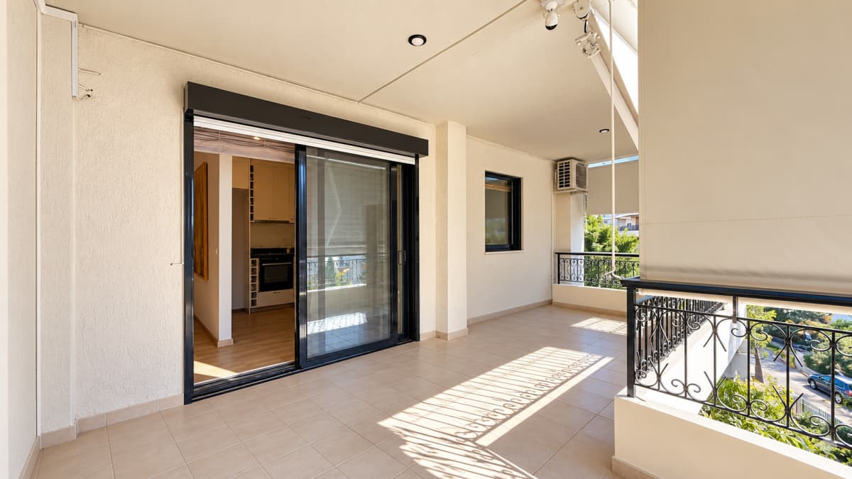 A wide tiled balcony with a black sliding glass door leading to an interior kitchen and a metal railing.