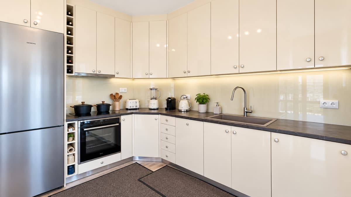 A modern kitchen with cream cabinets, a stainless steel refrigerator, and dark countertops.