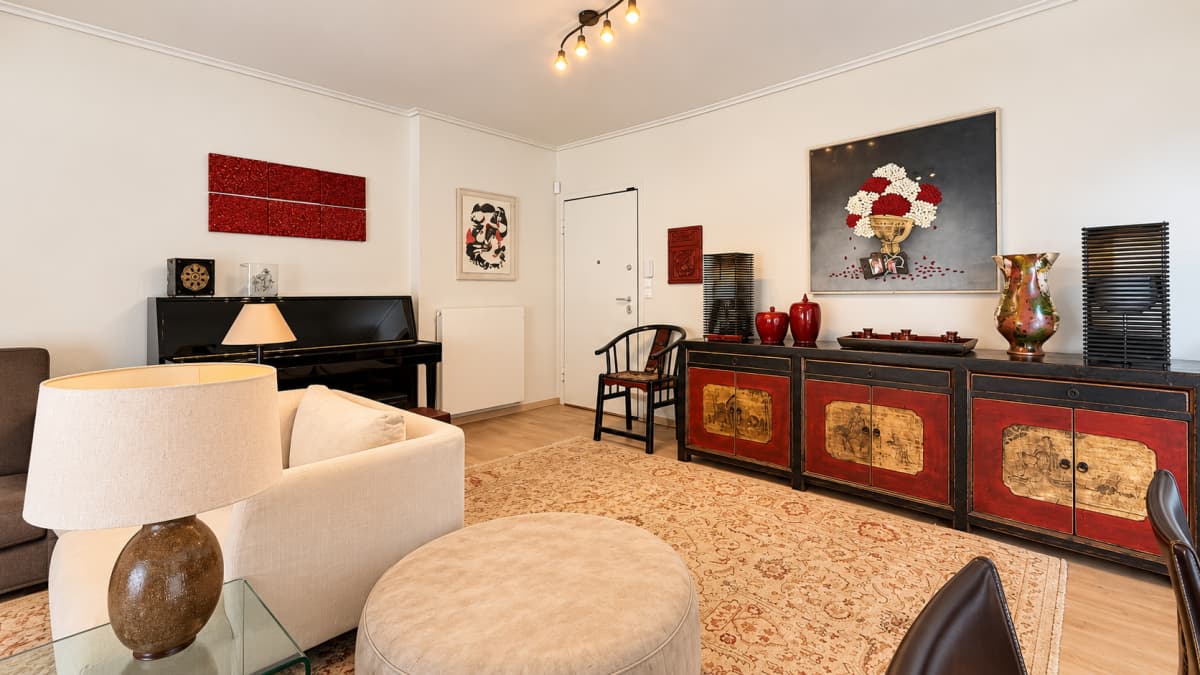 Living room furnished with a light-colored sofa, a piano, a round ottoman, and an ornate sideboard.