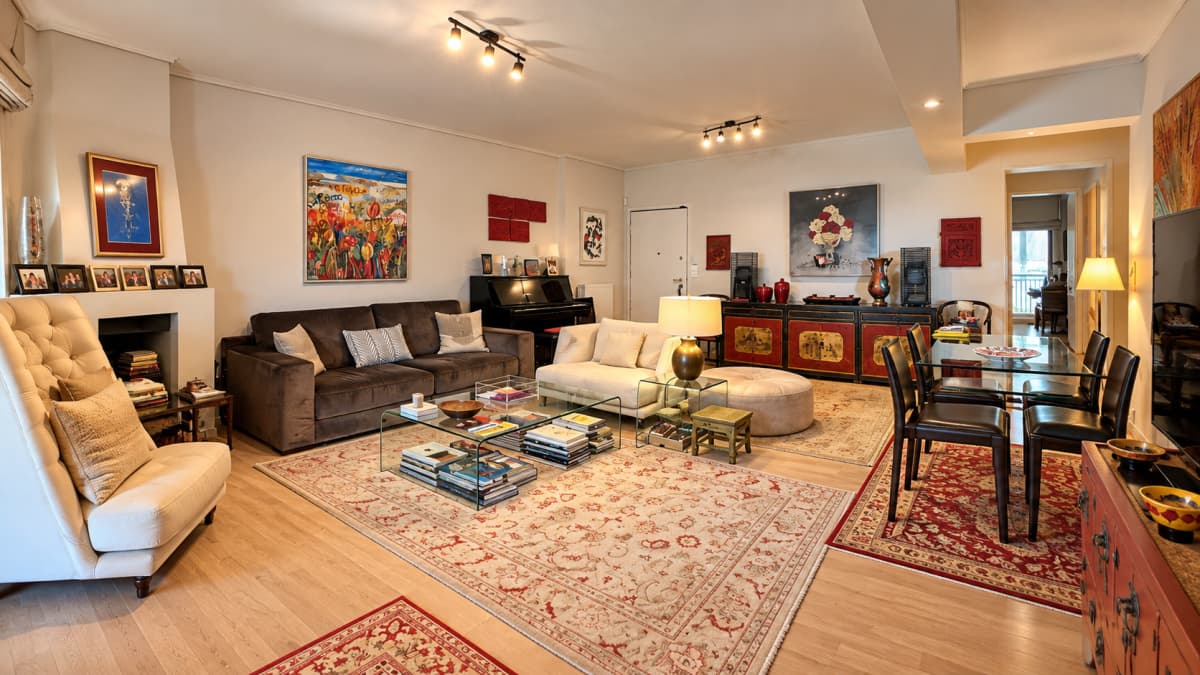 A wide interior view of a furnished living room with hardwood floors, rugs, sofas, a coffee table, and a dining area.