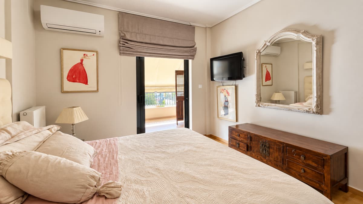 Bedroom featuring a large bed, a wooden dresser with a mirror, and a mounted television.