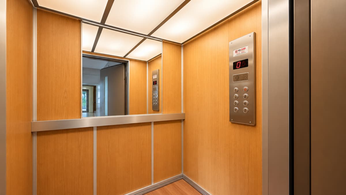 Inside of a wooden elevator cabin featuring a control panel and a mirror.
