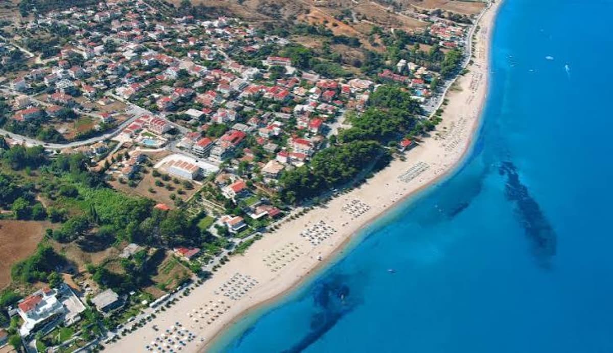 Εναέρια άποψη παραθαλάσσιας κωμόπολης με αμμώδη παραλία και γαλάζια θάλασσα.