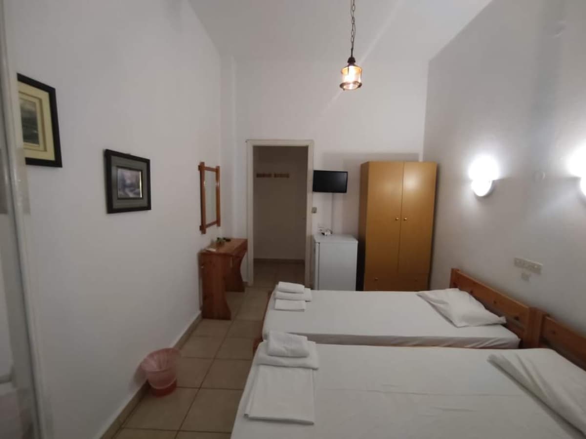 Δωμάτιο με δύο μονά κρεβάτια, ξύλινη ντουλάπα, μικρό ψυγείο και τηλεόραση.