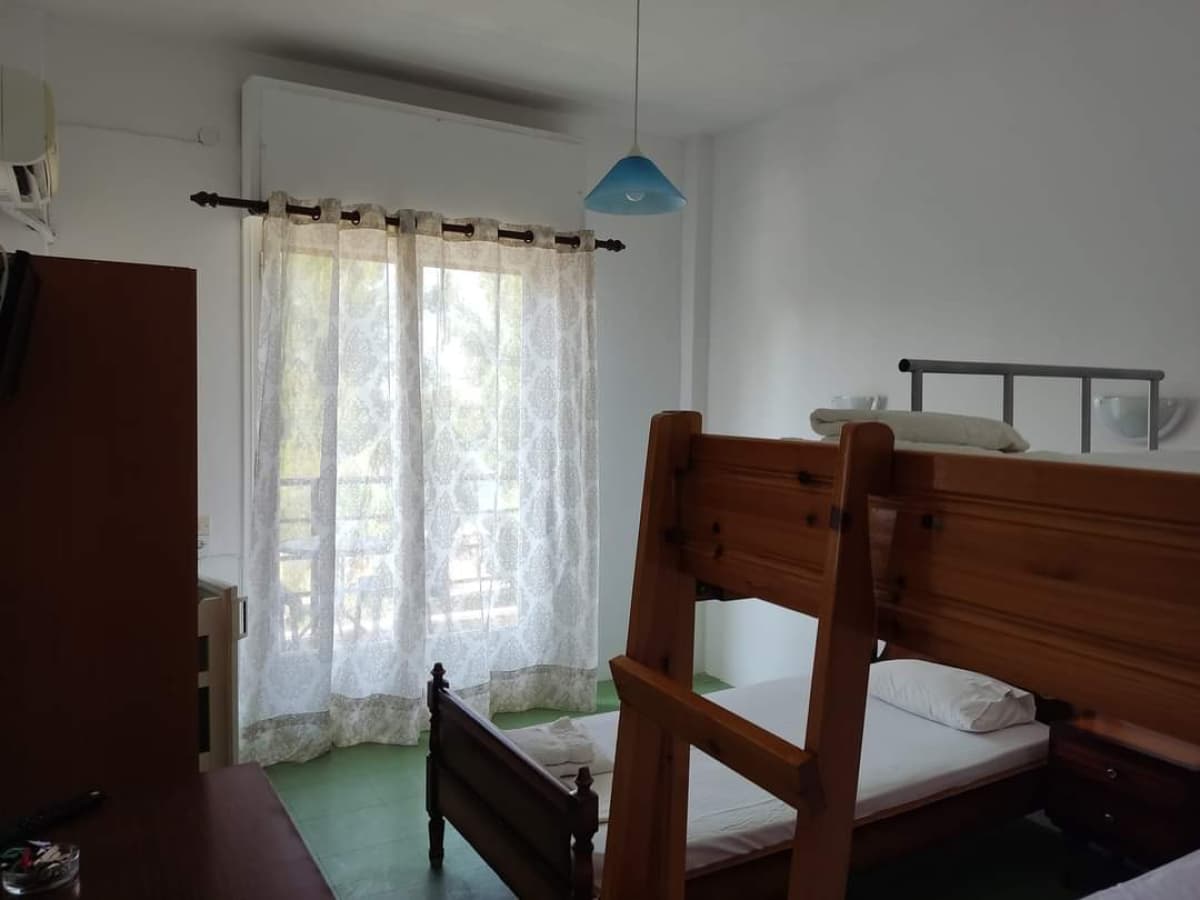 Υπνοδωμάτιο με ξύλινη κουκέτα, λευκά κλινοσκεπάσματα, παράθυρο με κουρτίνες και μπλε κρεμαστό φωτιστικό.
