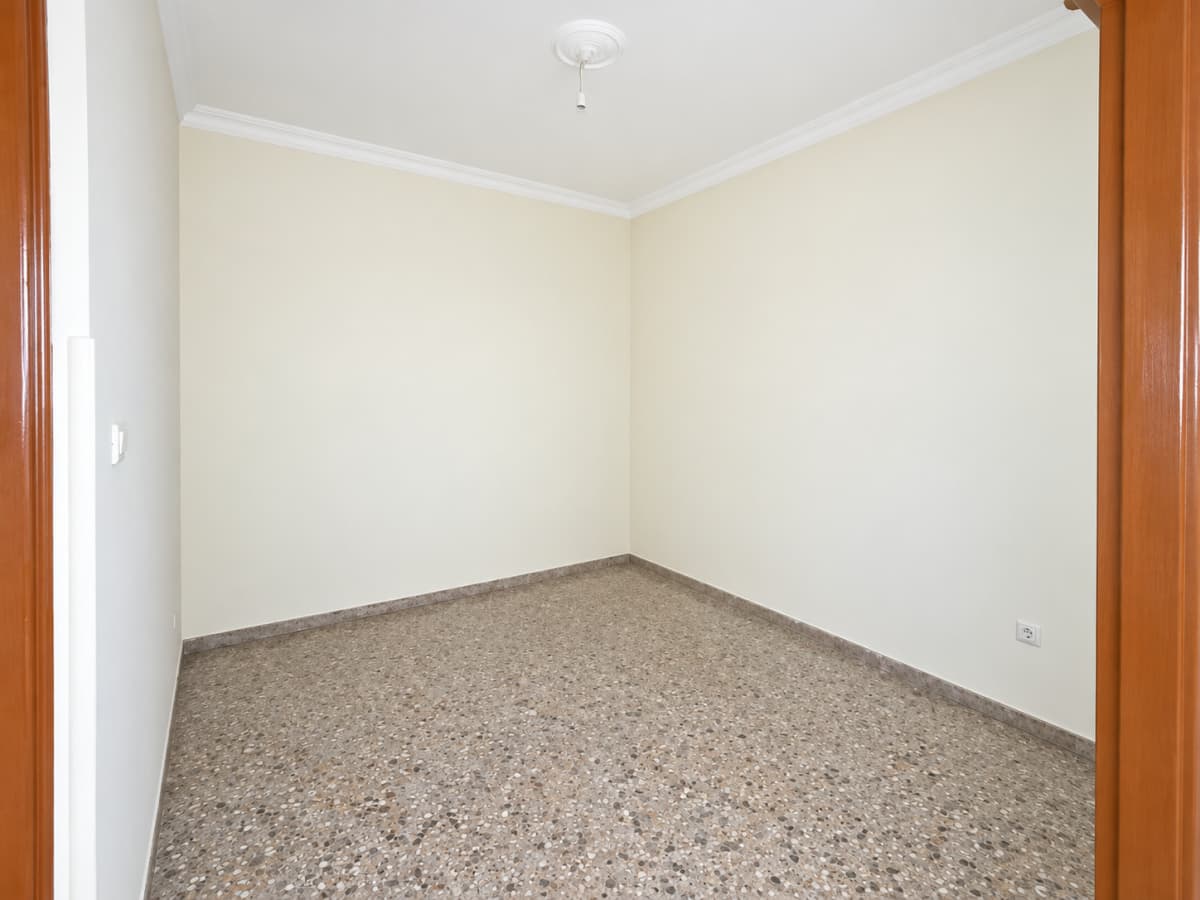 An empty room with light-colored walls, terrazzo flooring, and a ceiling light fixture, viewed through a doorway.