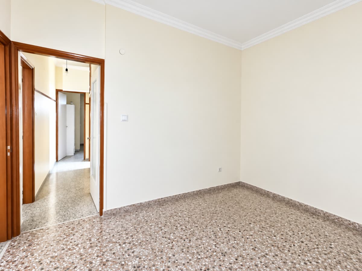 Empty room with cream-colored walls, patterned mosaic tile flooring, and an open doorway leading to a hallway.