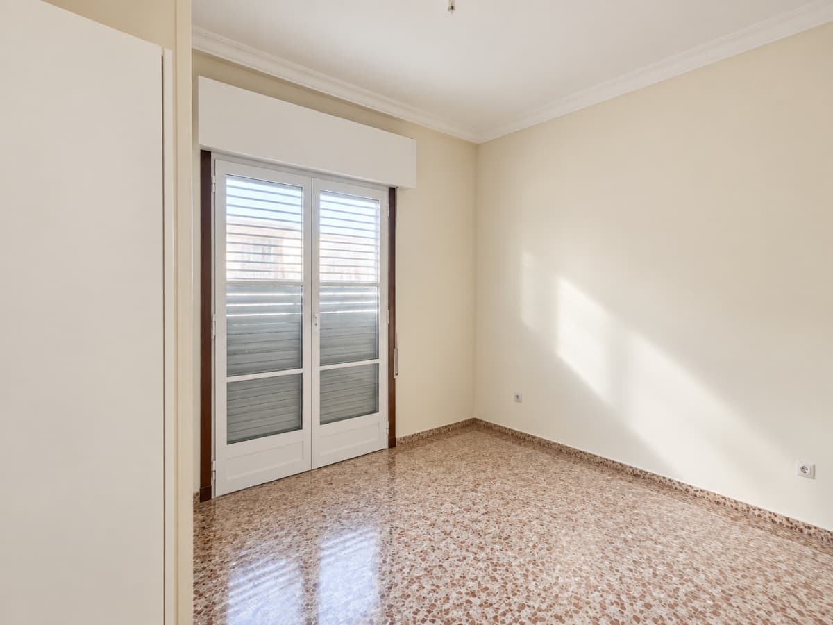 An empty room with beige walls, a brown patterned tile floor, and white double glass doors leading outside.