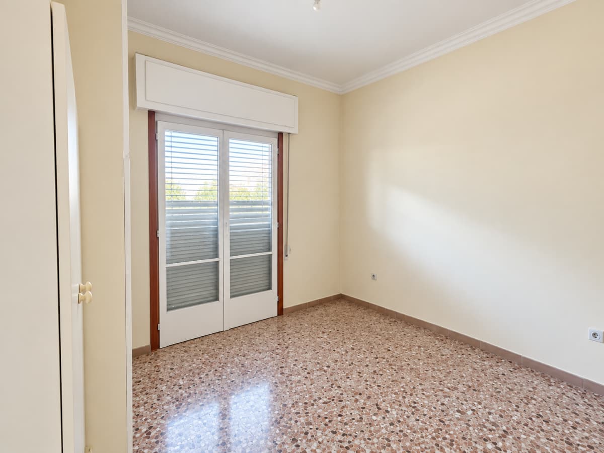 An empty room features light beige walls, a brown patterned tile floor, and a double glass door with blinds.