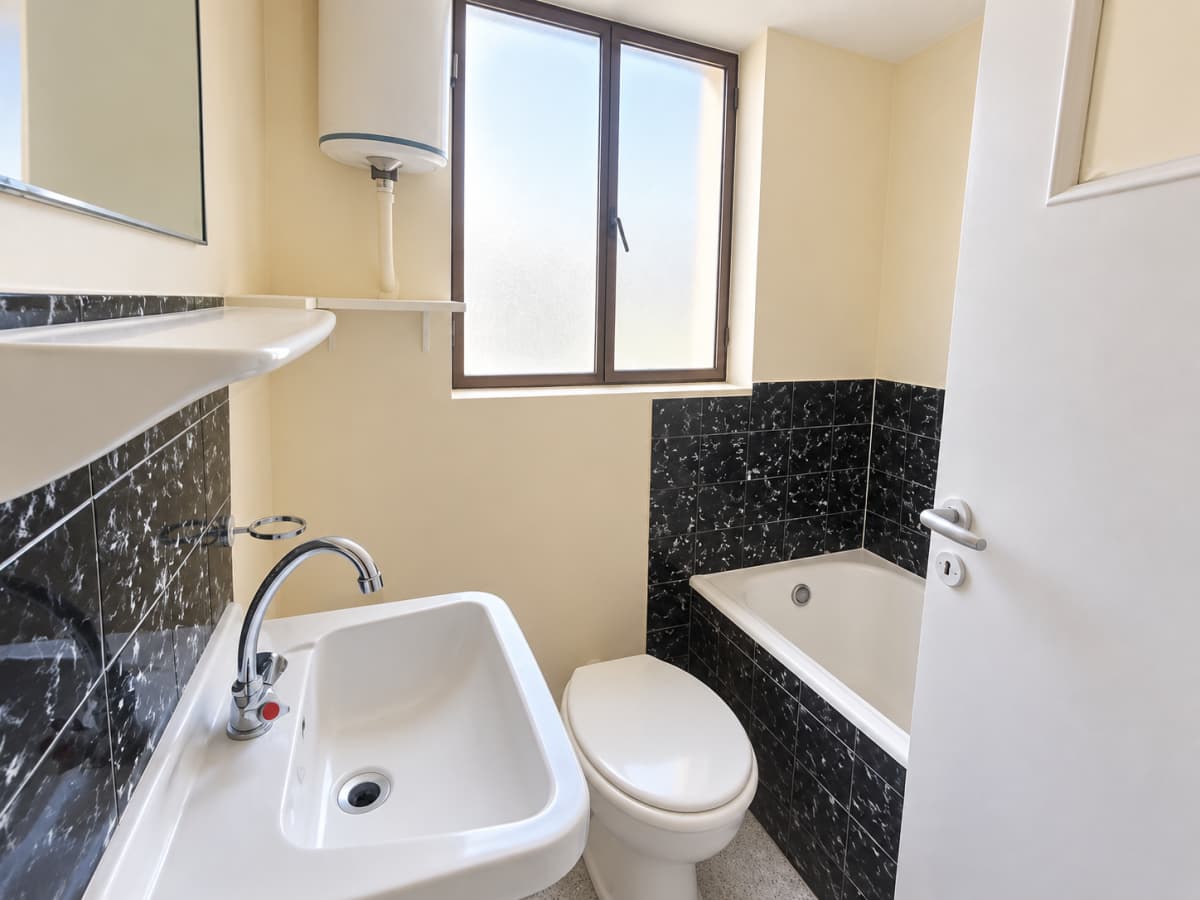 A compact bathroom featuring a white sink, toilet, and a bathtub tiled with black marble.
