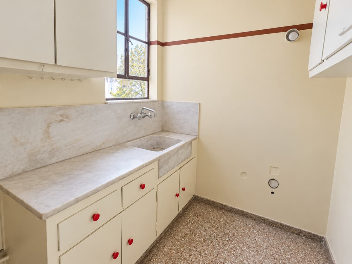 A kitchen featuring a marble countertop, sink, lower cabinets with red knobs, upper cabinets, a window, and patterned tile flooring.