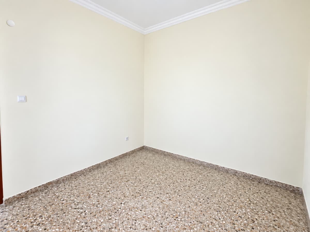 Corner of an empty room with light-colored walls and patterned stone flooring.