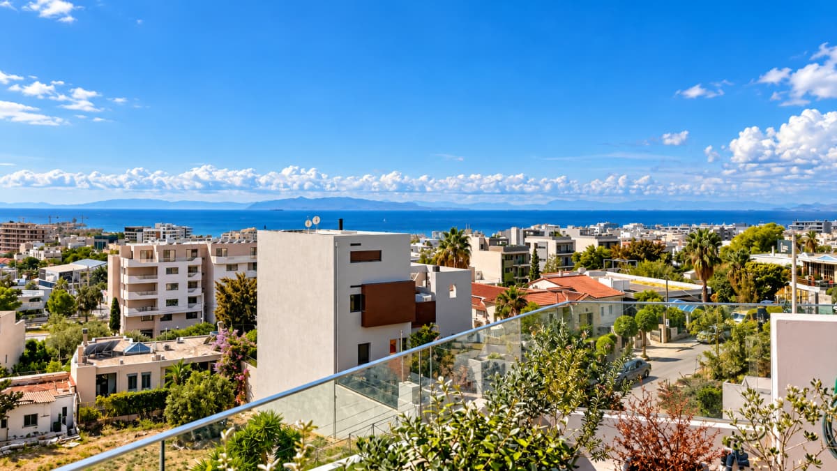 Ευρεία εξωτερική λήψη από μπαλκόνι με θέα σε παραθαλάσσια πόλη, κτίρια, δέντρα και θάλασσα κάτω από γαλάζιο ουρανό.