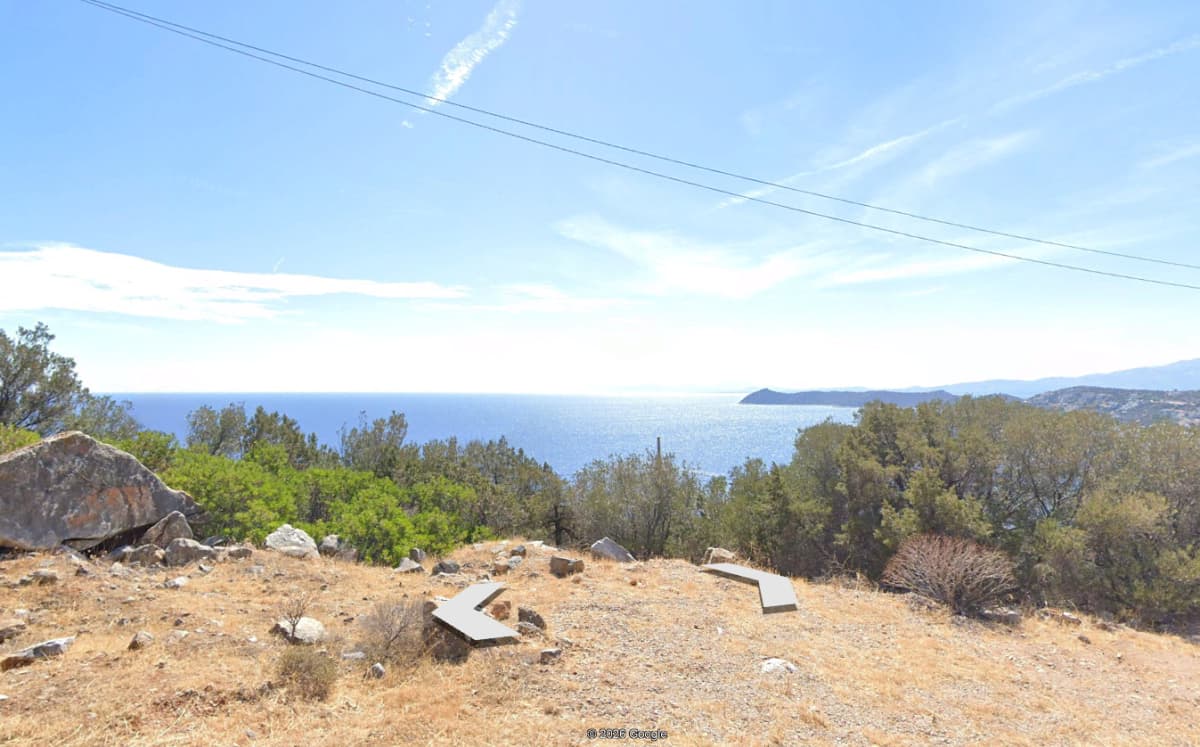 Εξωτερική θέα προς τη θάλασσα με λόφους στο βάθος και ξηρή, πετρώδη πλαγιά.