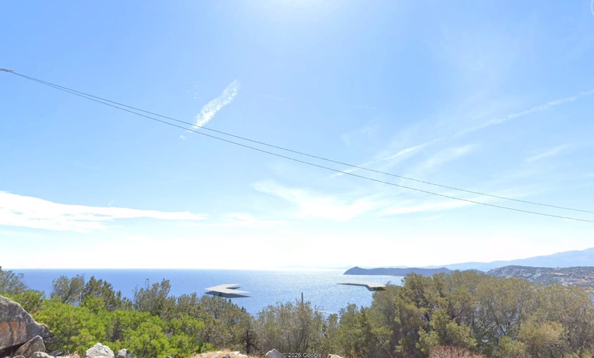 Υψίπεδη εξωτερική θέα δείχνει πράσινες κορυφές δέντρων στο προσκήνιο με θέα σε μια γαλάζια θάλασσα και μακρινά νησιά κάτω από φωτεινό ουρανό.