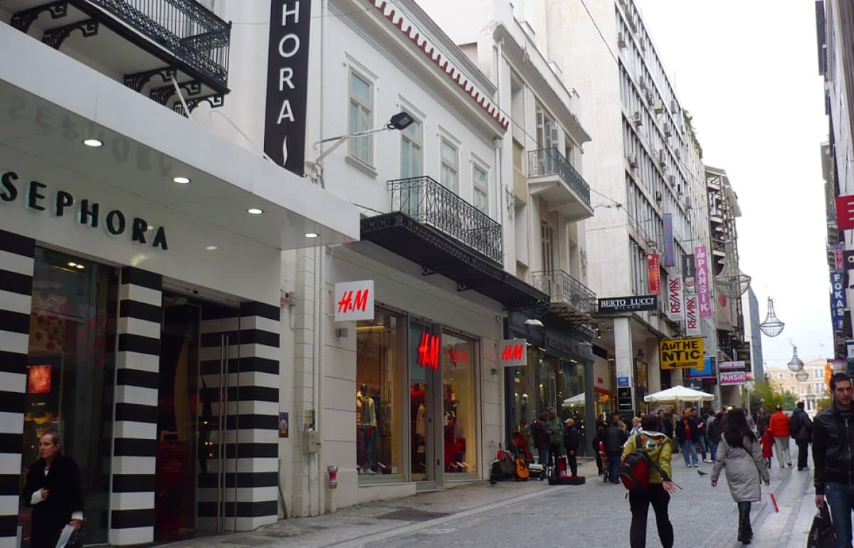 Εξωτερική άποψη εμπορικού δρόμου με καταστήματα και πεζούς.