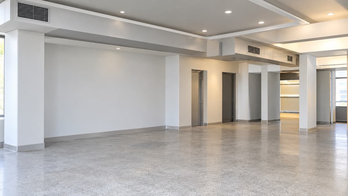 Όροφος γραφείων με λευκές κολόνες, χωνευτά φώτα οροφής και δάπεδο από μωσαϊκό.