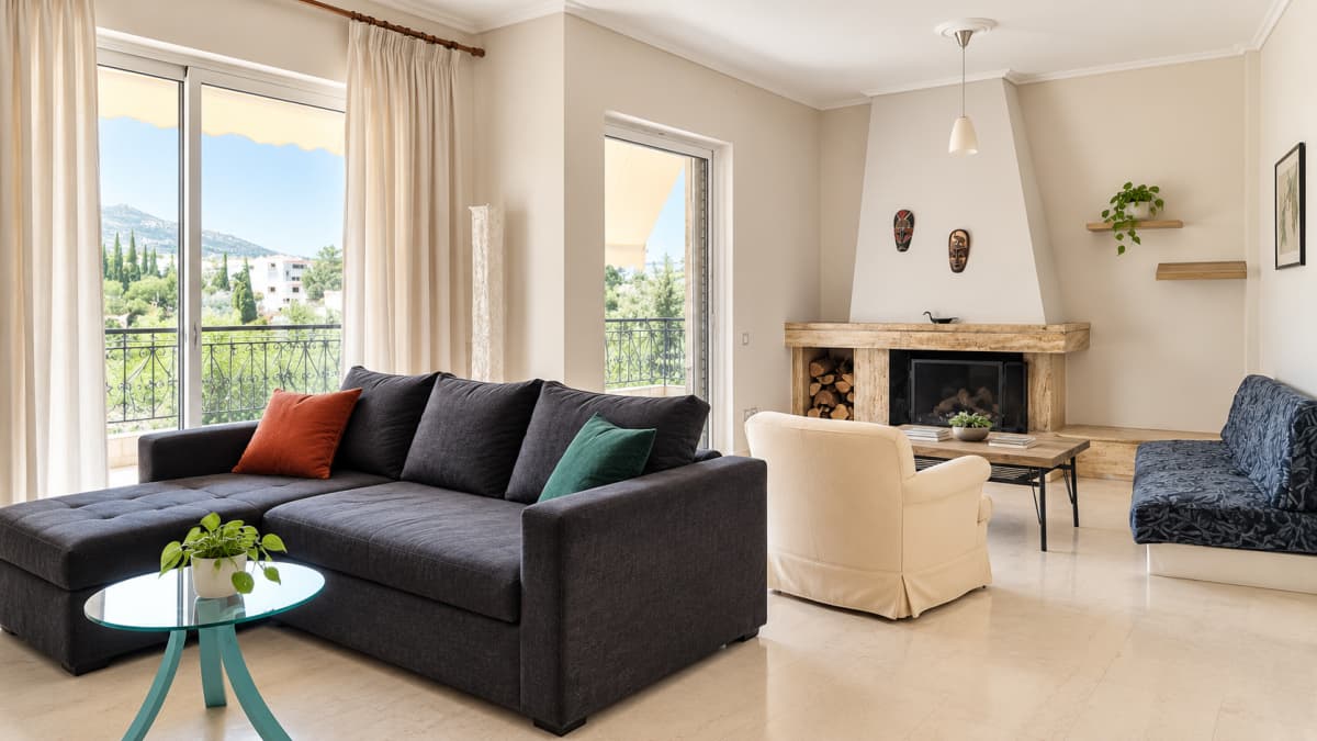 Living room with a corner sofa, an armchair and the fireplace, with tall windows to the balcony.