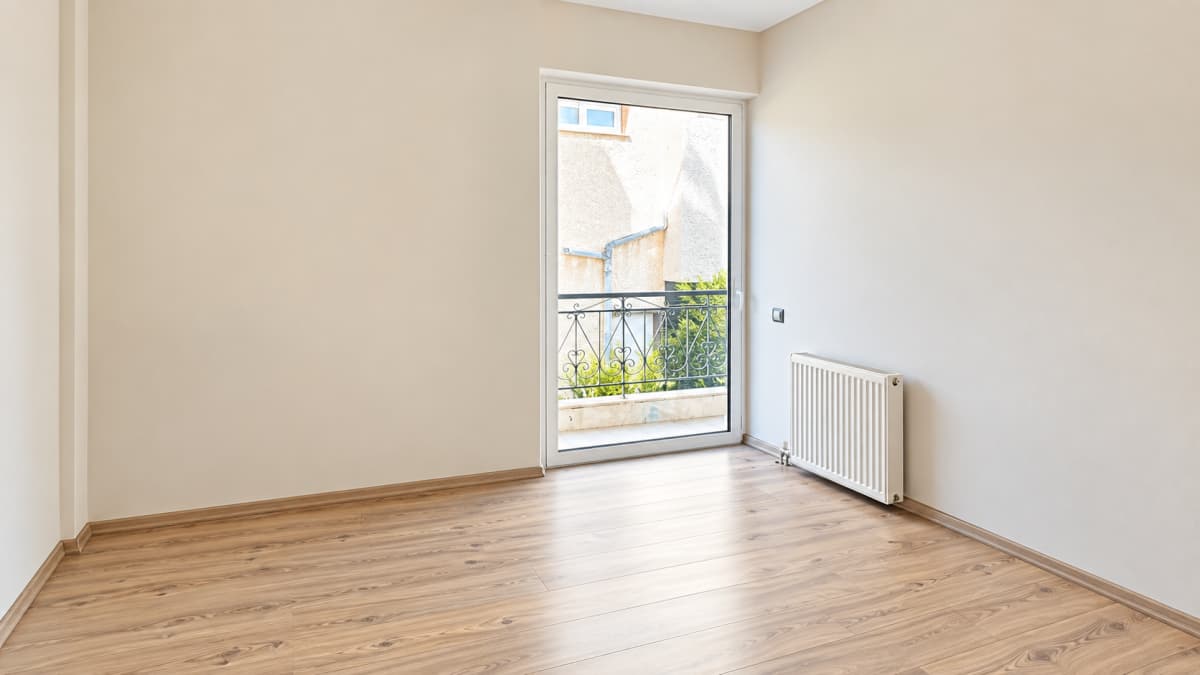 Empty bedroom with laminate flooring, a radiator and a glass door to the balcony.