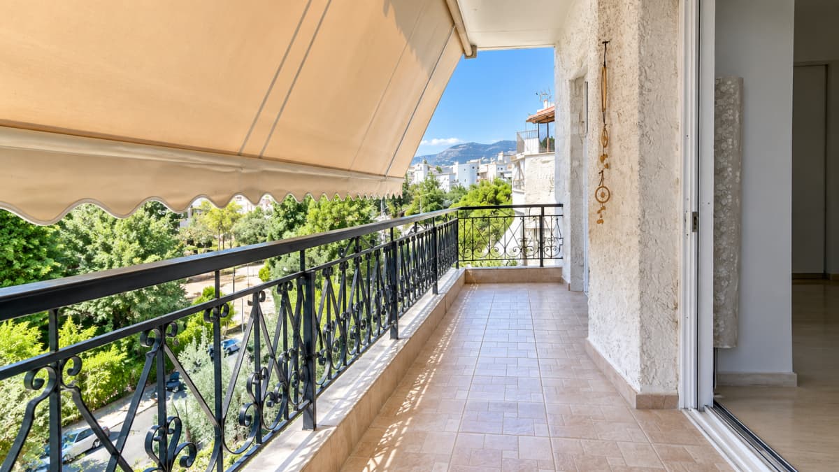 Long balcony with an awning and iron railings, looking over trees towards the mountains.