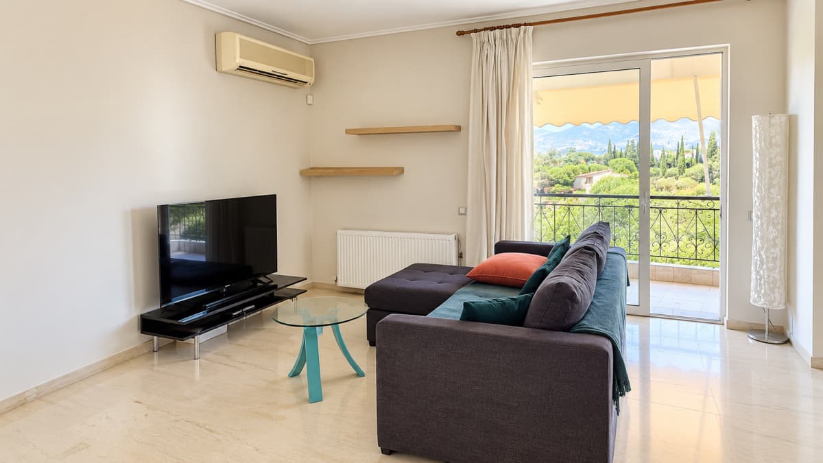 Sitting room with a sofa, a television and a glass door to the balcony with mountain views.