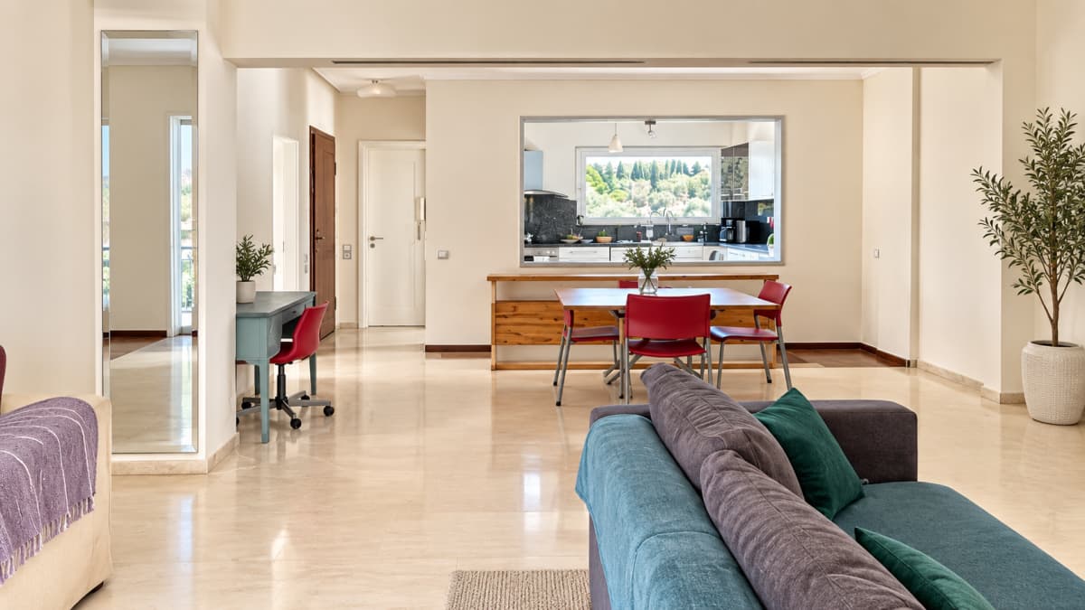 Open-plan living area with marble floors, a dining table and the kitchen through a serving hatch.