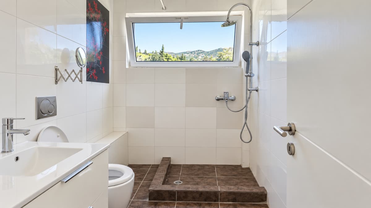 Bathroom with a walk-in shower, a wall-hung toilet and a vanity unit under a high window.