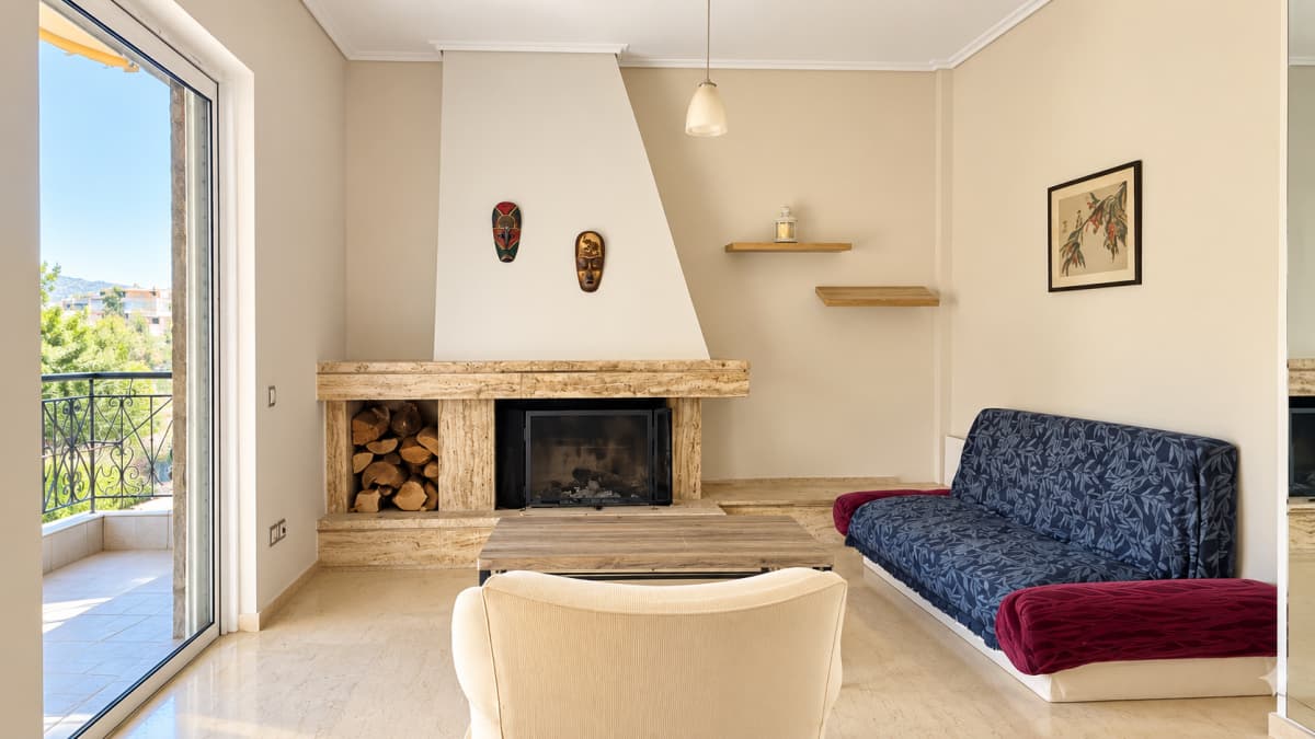Living room with a fireplace and log store, a sofa and armchair, and a glass door to the balcony.