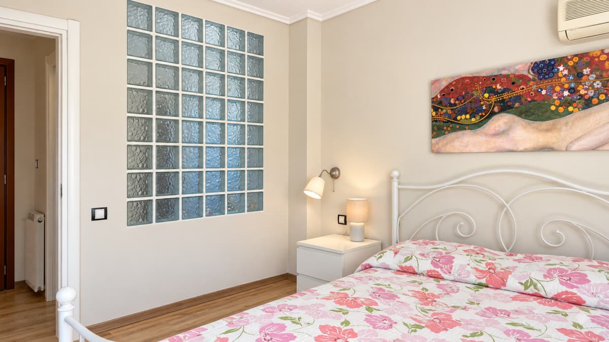 Bedroom with a glass-block wall panel, a white iron bed and laminate flooring.