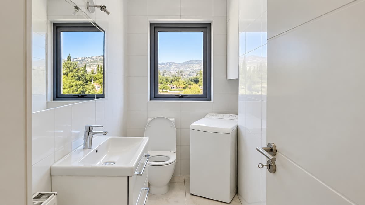 WC with a washbasin, a toilet and a washing machine, with two windows onto the hills.