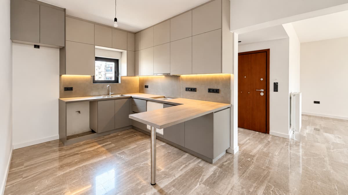 A modern kitchen with grey cabinetry, a light wood countertop, under-cabinet lighting, and marble tile flooring.