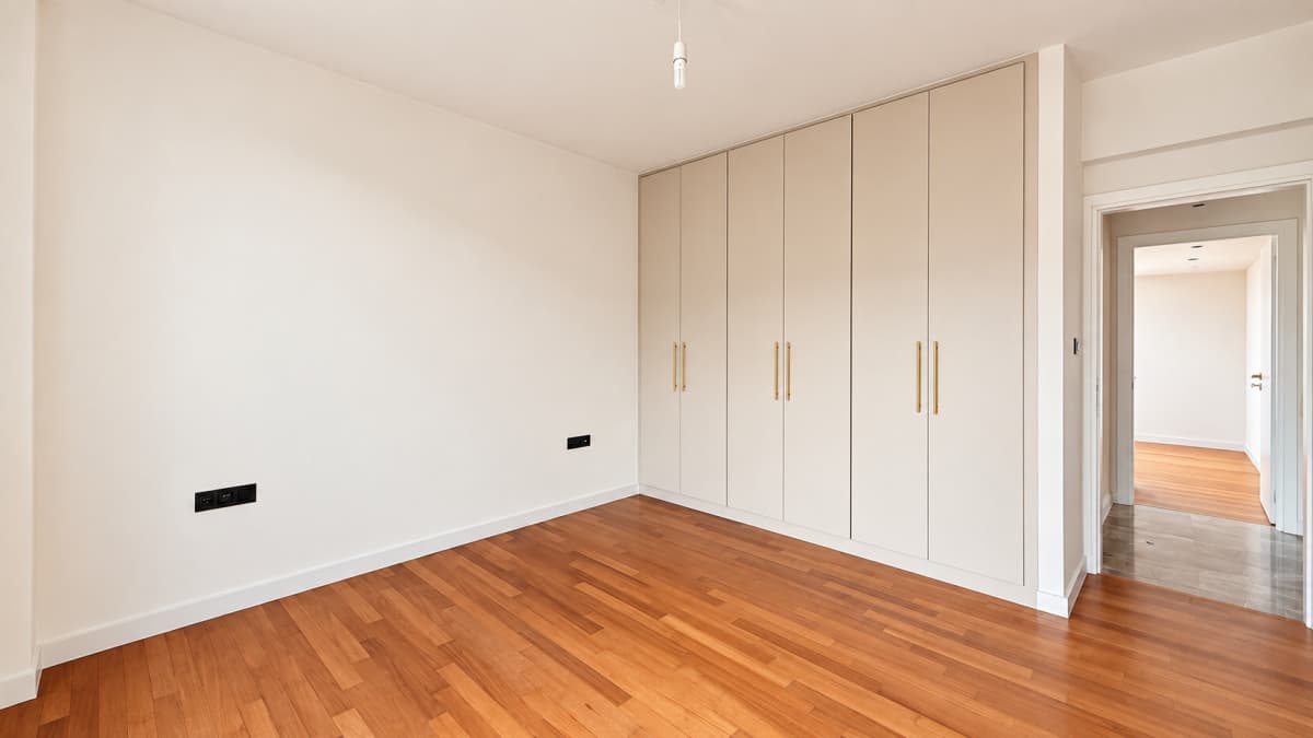An empty bedroom featuring wooden flooring, a built-in wardrobe, and a doorway leading to another room.