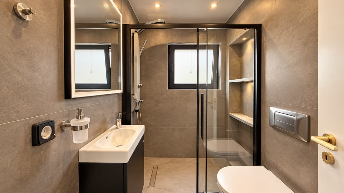 Modern bathroom featuring a walk-in shower enclosure, a wall-mounted sink with a vanity, and a toilet with grey tile walls and floors.