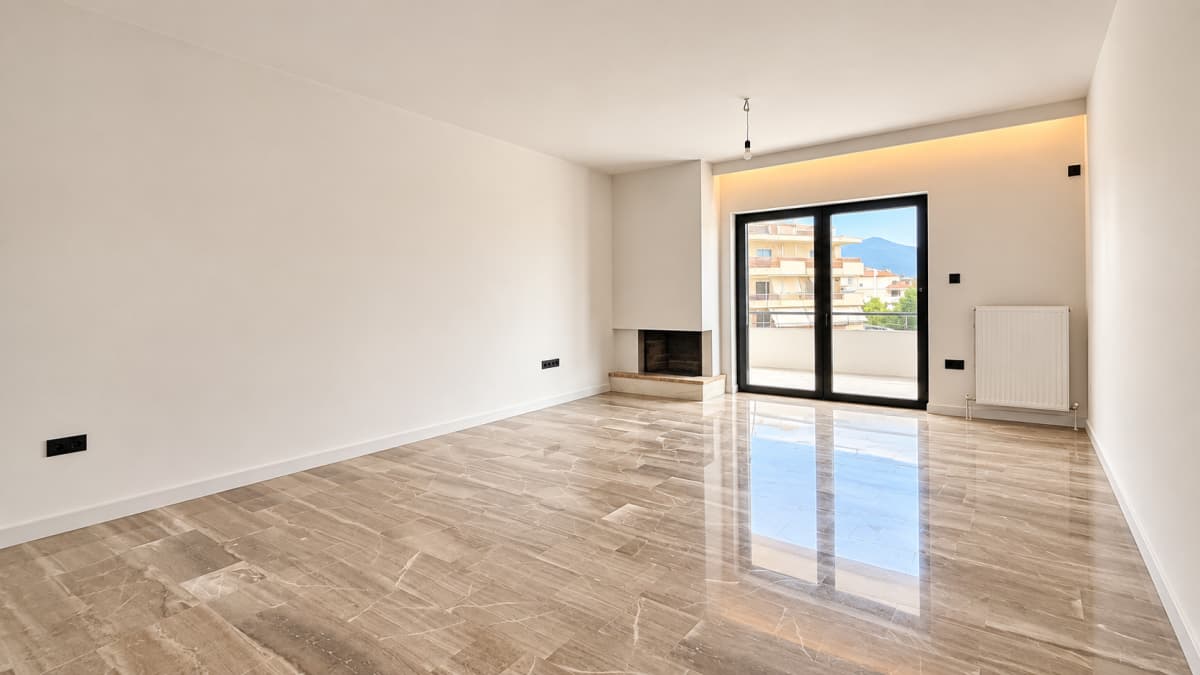 An empty room with polished marble flooring, white walls, a corner fireplace, a radiator, and large glass doors leading to a balcony.