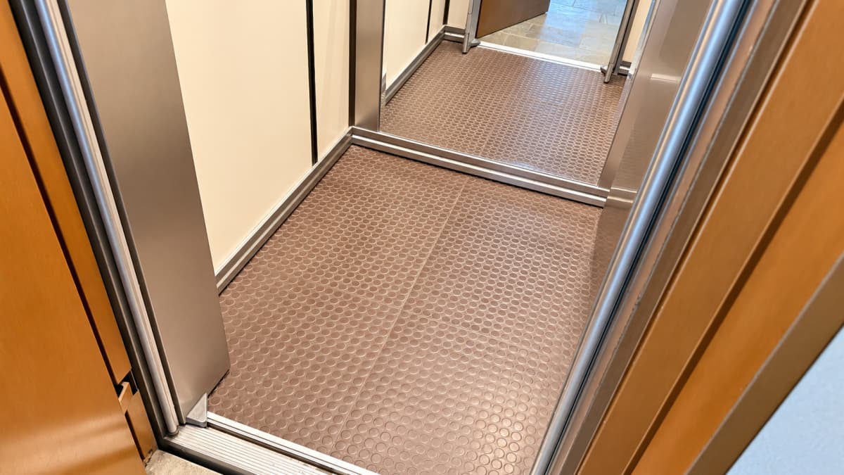 An elevator interior with brown circular-patterned flooring and metal door frames.