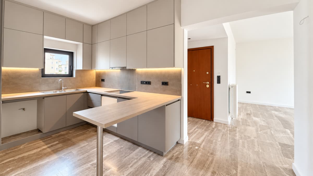 Modern kitchen with light grey cabinets, a wooden countertop with an integrated breakfast bar, and marble-look tile flooring.
