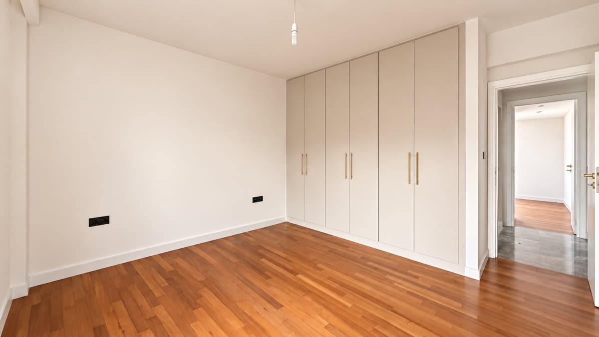 An empty room with hardwood flooring, beige walls, built-in wardrobes, and an open doorway.