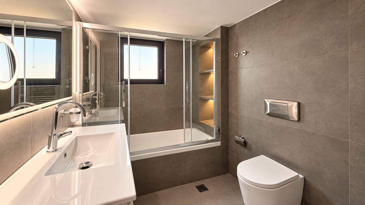 Modern bathroom with a white sink in the foreground, a bathtub with glass sliding doors, and a wall-hung toilet on the right.
