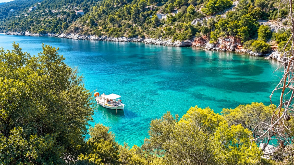 Elevated view of a bay with turquoise waters, a boat, and lush green hills.