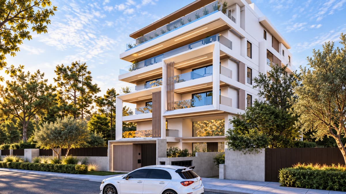 Exterior view of a modern multi-story residential building with white balconies and large windows, fronted by a street with a parked white car and surrounding trees.