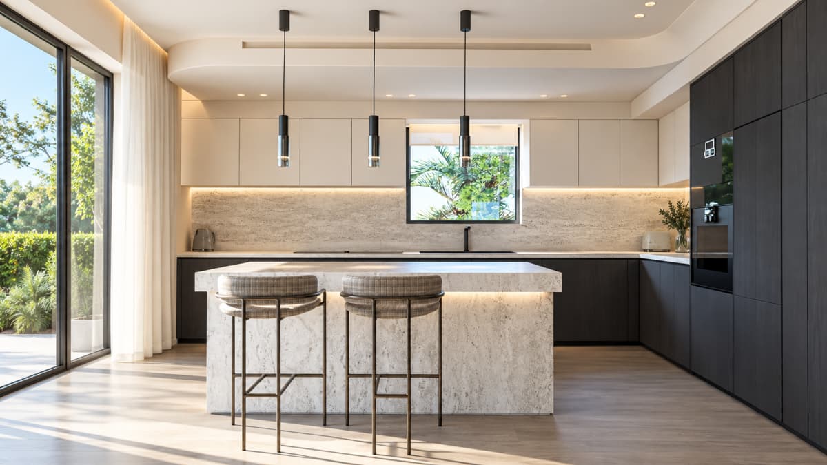 A modern kitchen featuring a marble island, two bar stools, dark wooden cabinetry, and large sliding glass doors opening to a garden.