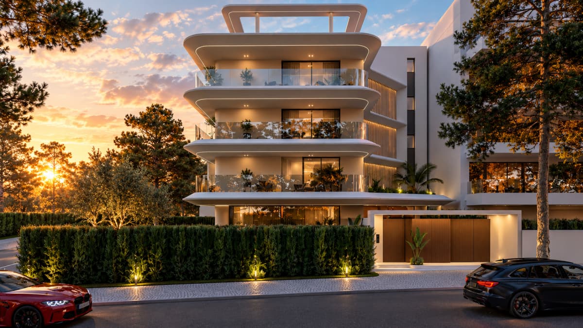 Exterior view of a modern multi-story residential building with rounded balconies at sunset, featuring a hedge fence, a wooden entrance gate, and cars parked in front.