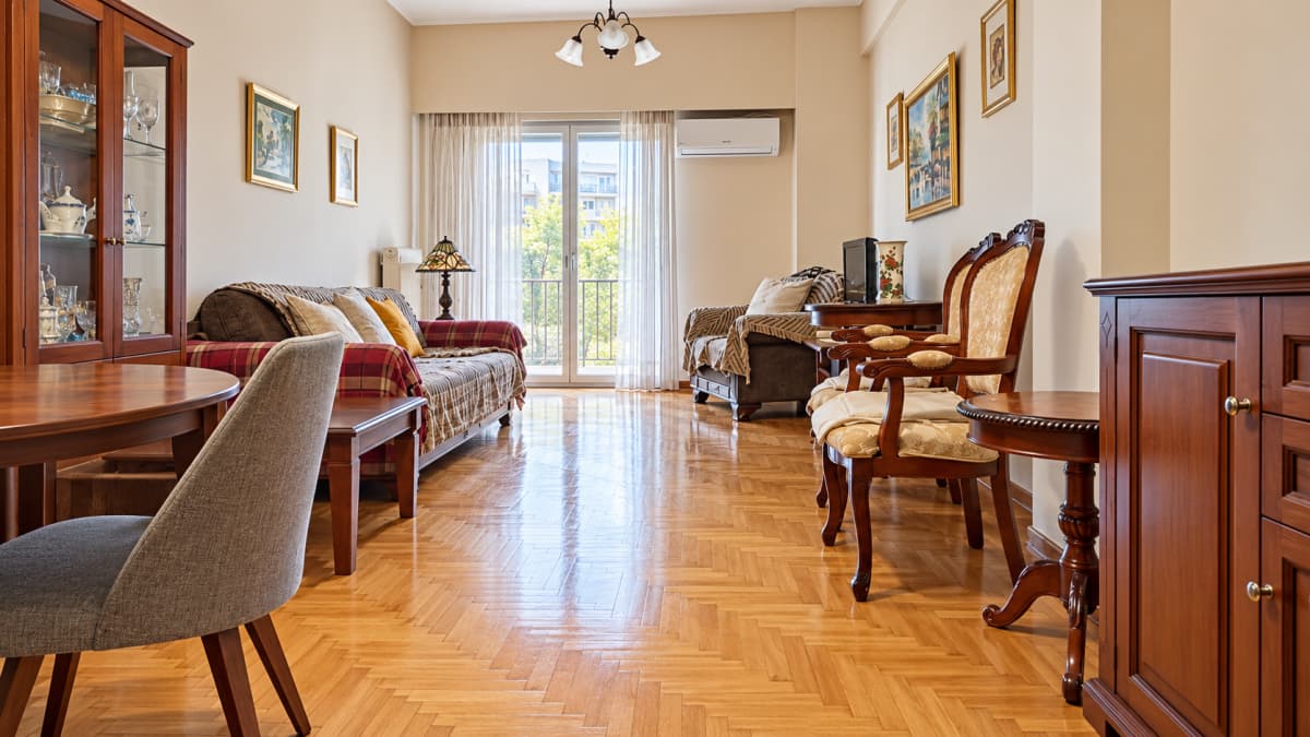 Σαλόνι με παρκέ δάπεδο, καναπέ στα αριστερά, πολυθρόνες στα δεξιά και τραπεζία.