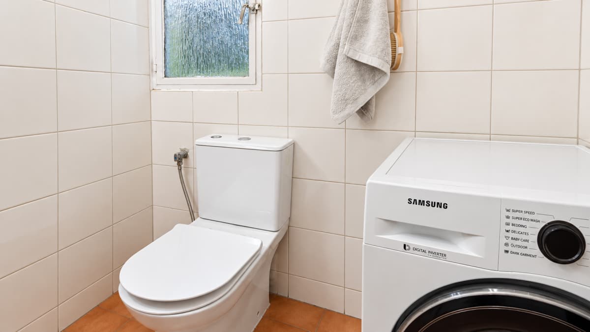 Μinimalistic bathroom with toilet, washing machine, and tiled walls.