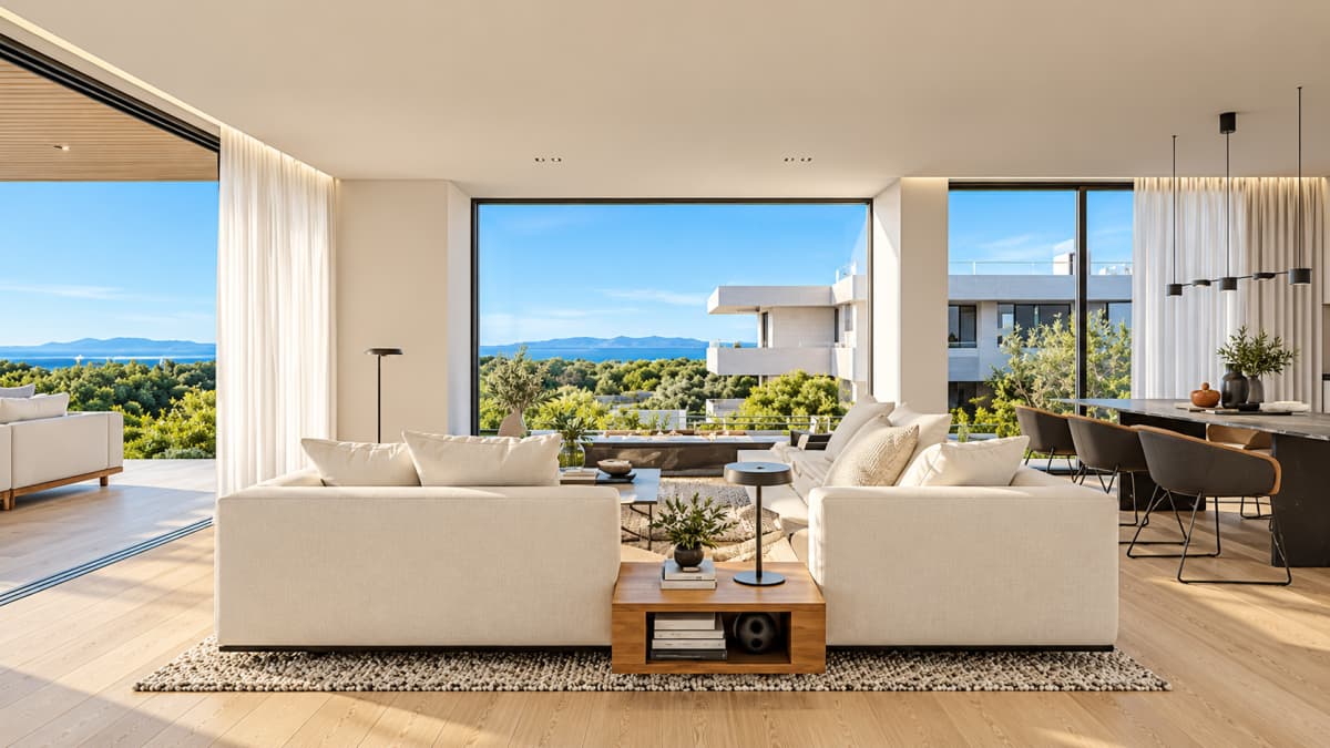 A modern living room featuring two cream-colored sectional sofas facing a large window with a scenic view of trees and the sea.